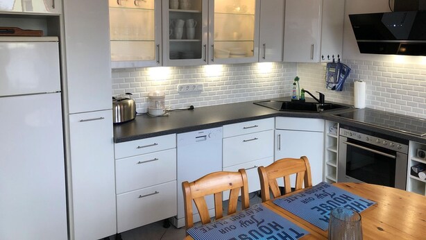 Una cocina moderna con armarios blancos, horno integrado y comedor con mesa y sillas de madera.