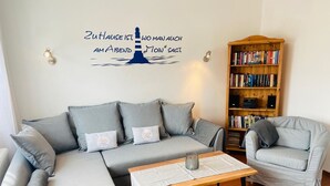 Una sala de estar con un sofá seccional gris, una mesa de centro de madera, un sillón gris y una estantería llena de libros y dispositivos electrónicos.