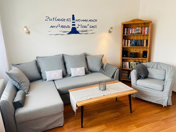 A living room with a grey sectional sofa, a wooden coffee table, a grey armchair, and a bookshelf filled with books and electronic devices.