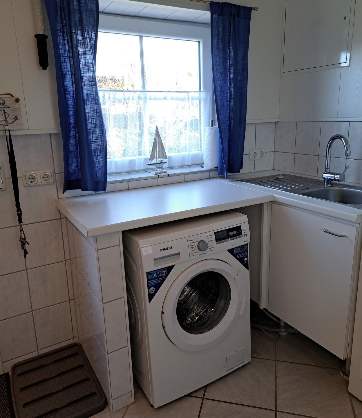 A compact kitchen with a washing machine, a sink, and a window with curtains.