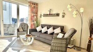 A living room with a grey sofa, wicker chairs, a glass coffee table, and a floor lamp.