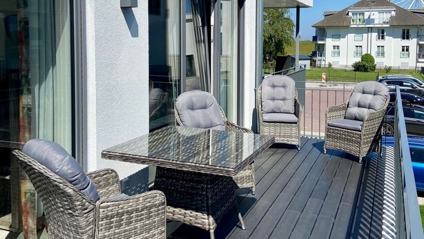 A modern building with a balcony featuring wicker furniture and a glass table.