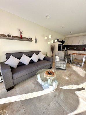 Una sala moderna con un sofá gris, una mesa de centro de vidrio y una silla de mimbre.
