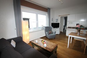 Ein modernes Wohnzimmer mit einer Couch, einem Couchtisch mit Früchten, einem grauen Sessel und einem Essbereich mit einem weißen Tisch und Stühlen.