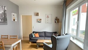 Ein modernes Wohnzimmer mit grauem Sofa, einem Holztisch und einem Essbereich mit Holztisch und Stühlen.