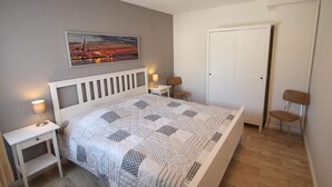 Ein Schlafzimmer mit Bett, Nachttischen, einem Sessel und einer Tür.