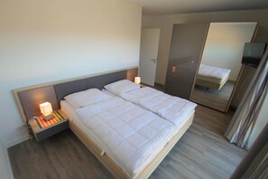 Une chambre d’hôtel avec un grand lit, des tables de chevet avec des lampes, un miroir et un téléviseur.