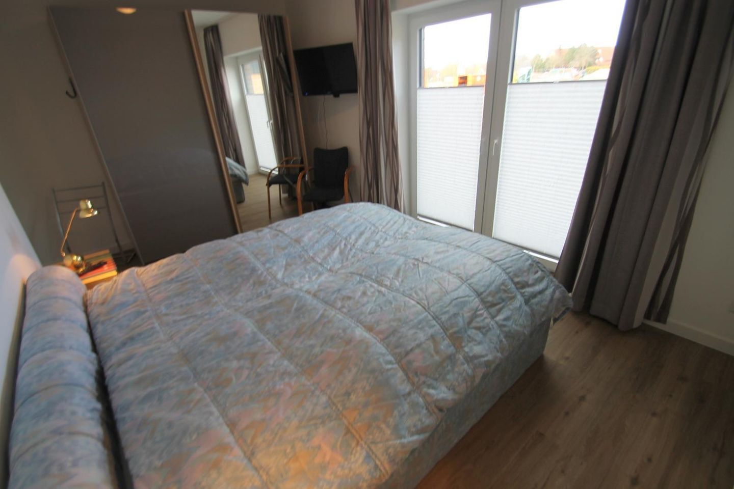Une chambre à coucher avec un lit, un bureau, une chaise, un téléviseur et une fenêtre avec des rideaux.