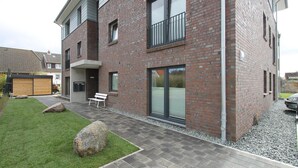A modern two-story building with a brick facade, large windows, and a small outdoor seating area with a bench.