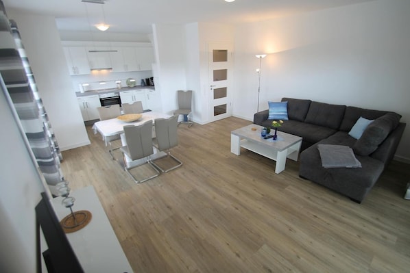 Una sala de estar moderna con un sofá gris, una mesa de centro y una zona de comedor con una mesa y sillas blancas.