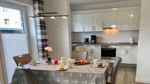 A modern kitchen with white cabinets, a coffee maker, and a dining table set for four with a grey tablecloth featuring anchor patterns.