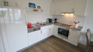 Una cocina moderna con armarios blancos, lavavajillas, estufa y cafetera.