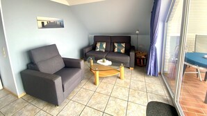 A living room with a sofa, armchair, and coffee table. There is a painting on the wall and a lamp on a side table.