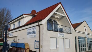 A white building with a red roof, labeled "Strandkörbe," featuring a sign for "Strand Café & Restaurant."