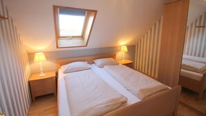 A bedroom with a double bed, two bedside tables with lamps, a skylight, and a mirror on the wall.