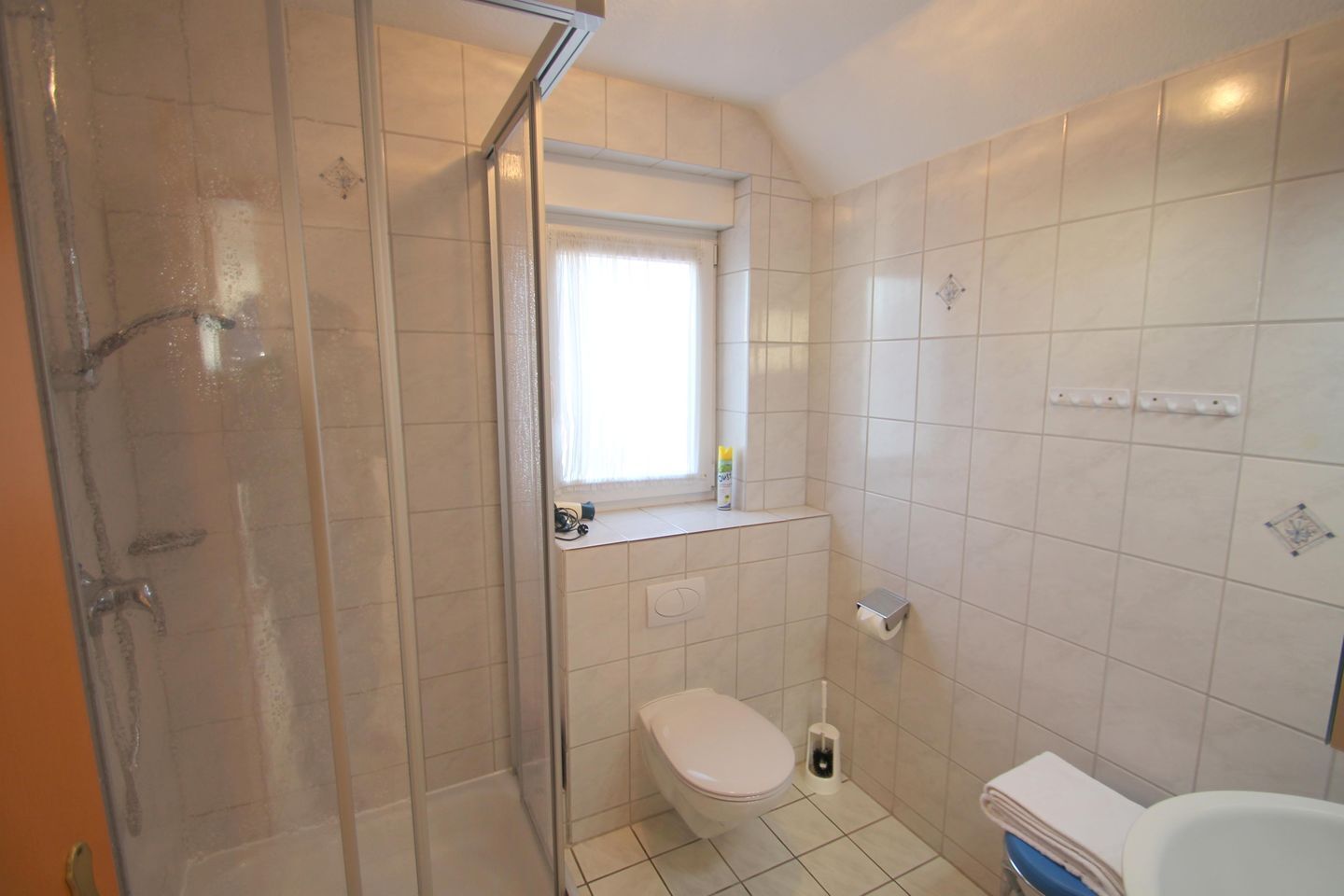 Et lille badeværelse med toilet, bruser og et vindue.