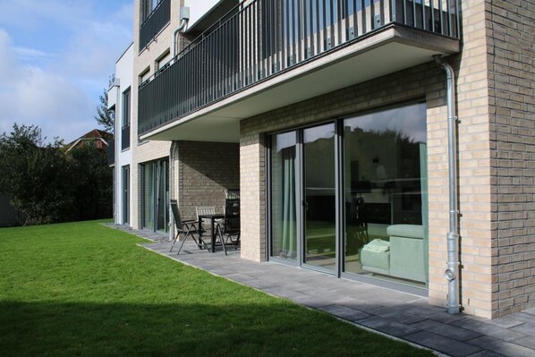 Une maison moderne à deux étages, dotée d’un balcon, de portes-fenêtres coulissantes et d’une pelouse bien entretenue.