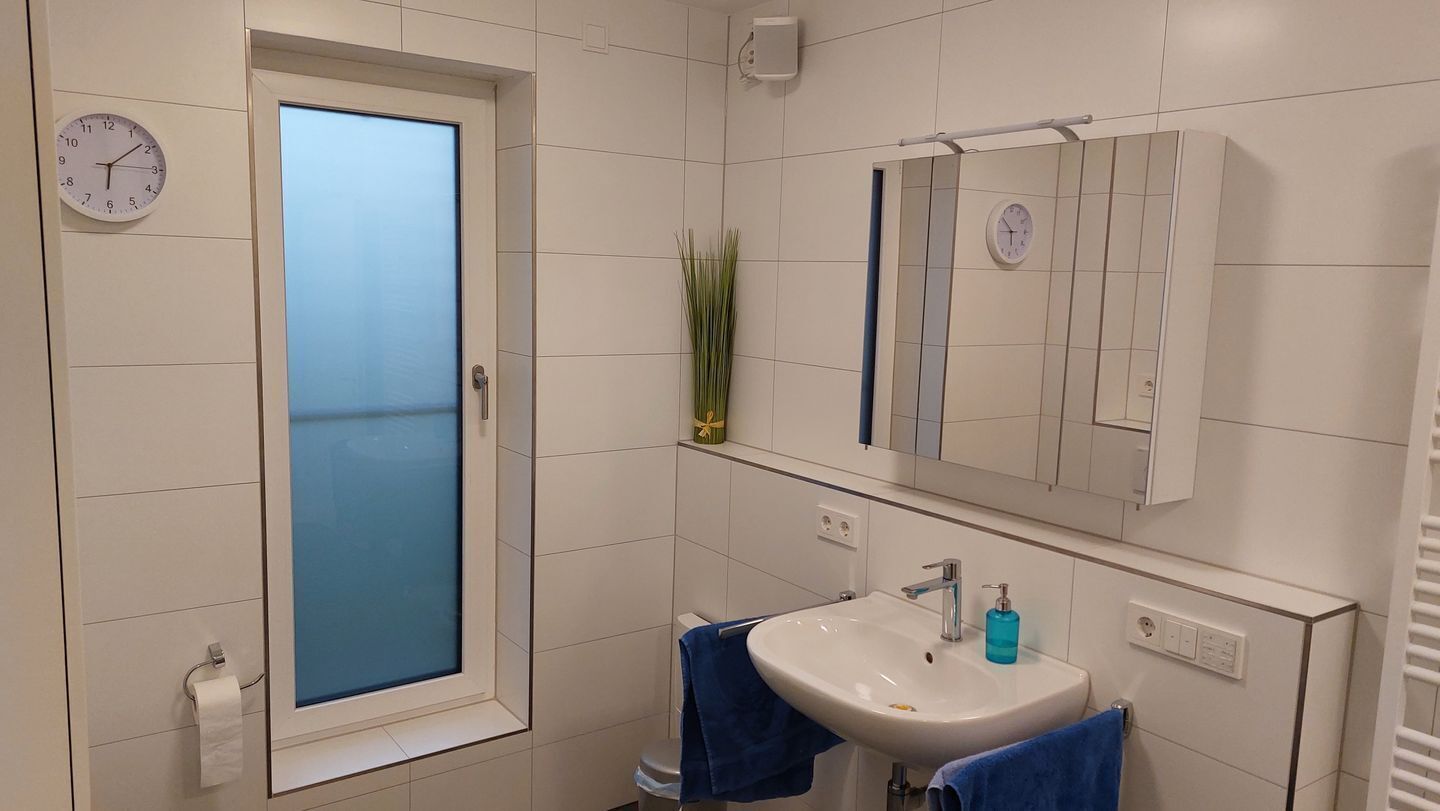 Ein Badezimmer mit einem weißen Waschbecken, zwei blauen Handtüchern, einem Spiegel und einer Uhr an der Wand.
