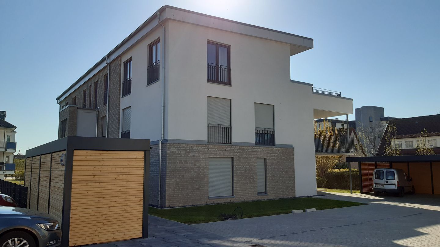 A modern two-story residential building with a flat roof, large windows, and a small balcony.