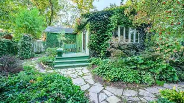 A garden with a stone pathway leading to a wooden bench and a small shed.