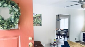 A living room with a red door, a blue sofa, a dining area with a table and chairs, and a ceiling fan.