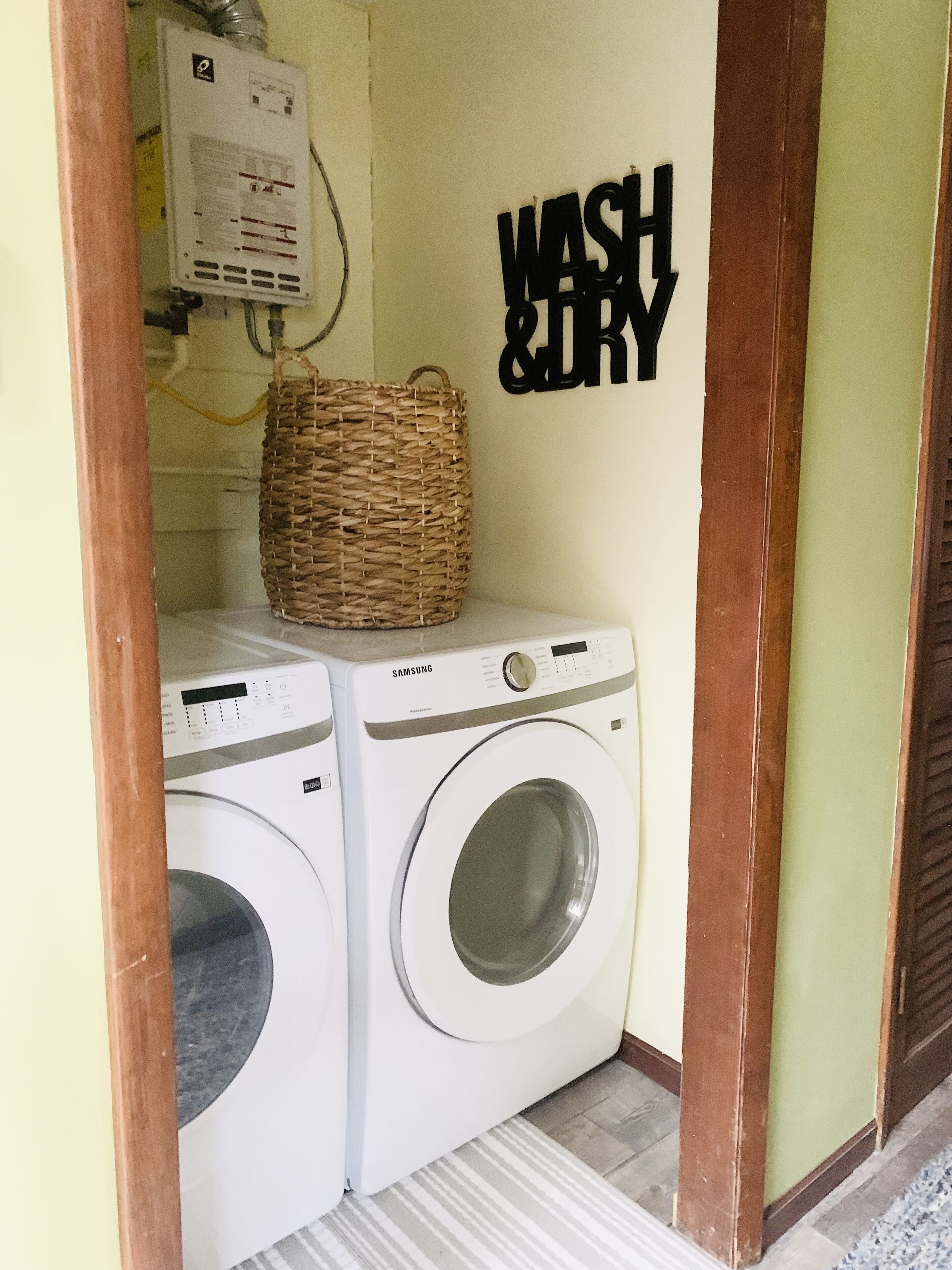 Un espace buanderie avec deux machines à laver Samsung blanches, un panier en osier posé sur le dessus, et un panneau mural indiquant « LAVAGE ET SÉCHAGE ».