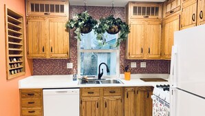 A kitchen with wooden cabinets, a white countertop, a dishwasher, a sink, and hanging plants.