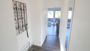 Un pasillo con una obra de arte rústica en la pared, un perchero metálico y vistas a un balcón.