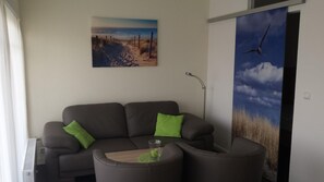 A modern living room with a grey sofa, a small coffee table, and a painting of a beach scene. - 1515 - Dünenresidenz WG 5 - Dünenresidenz apartment 5 (Dahme)