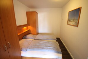 A small, compact room with two beds, a wooden wardrobe, and a painting on the wall. - 1515 - Dünenresidenz WG 5 - Dünenresidenz apartment 5 (Dahme)