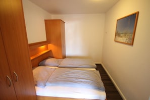 A small, compact room with two beds, a wooden wardrobe, and a painting on the wall. - 1515 - Dünenresidenz WG 5 - Dünenresidenz apartment 5 (Dahme)