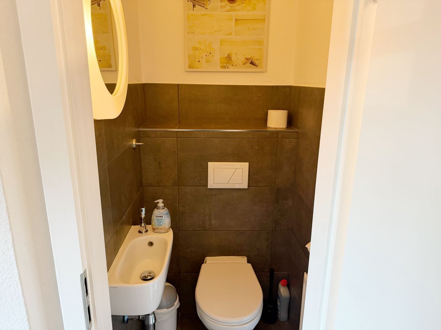 Un baño con lavamanos, inodoro y dispensador de papel higiénico en la pared.