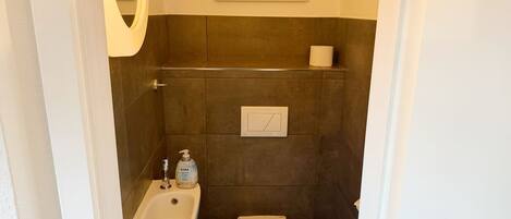 Un baño con lavamanos, inodoro y dispensador de papel higiénico en la pared.