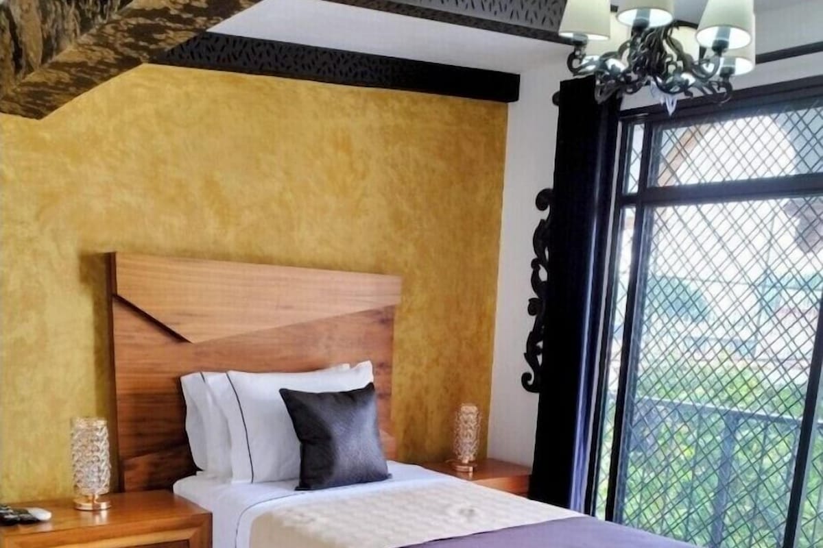Ein Schlafzimmer mit einem hölzernen Bett, einem Nachttisch und Blick ins Freie durch ein Fenster.