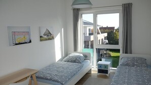 Une chambre avec deux lits, un bureau et un balcon donnant sur une maison et un jardin.