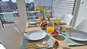 Une table de petit-déjeuner dressée avec des assiettes, des couverts, des verres de jus d’orange, un bol de cerises et un vase rempli de fleurs.