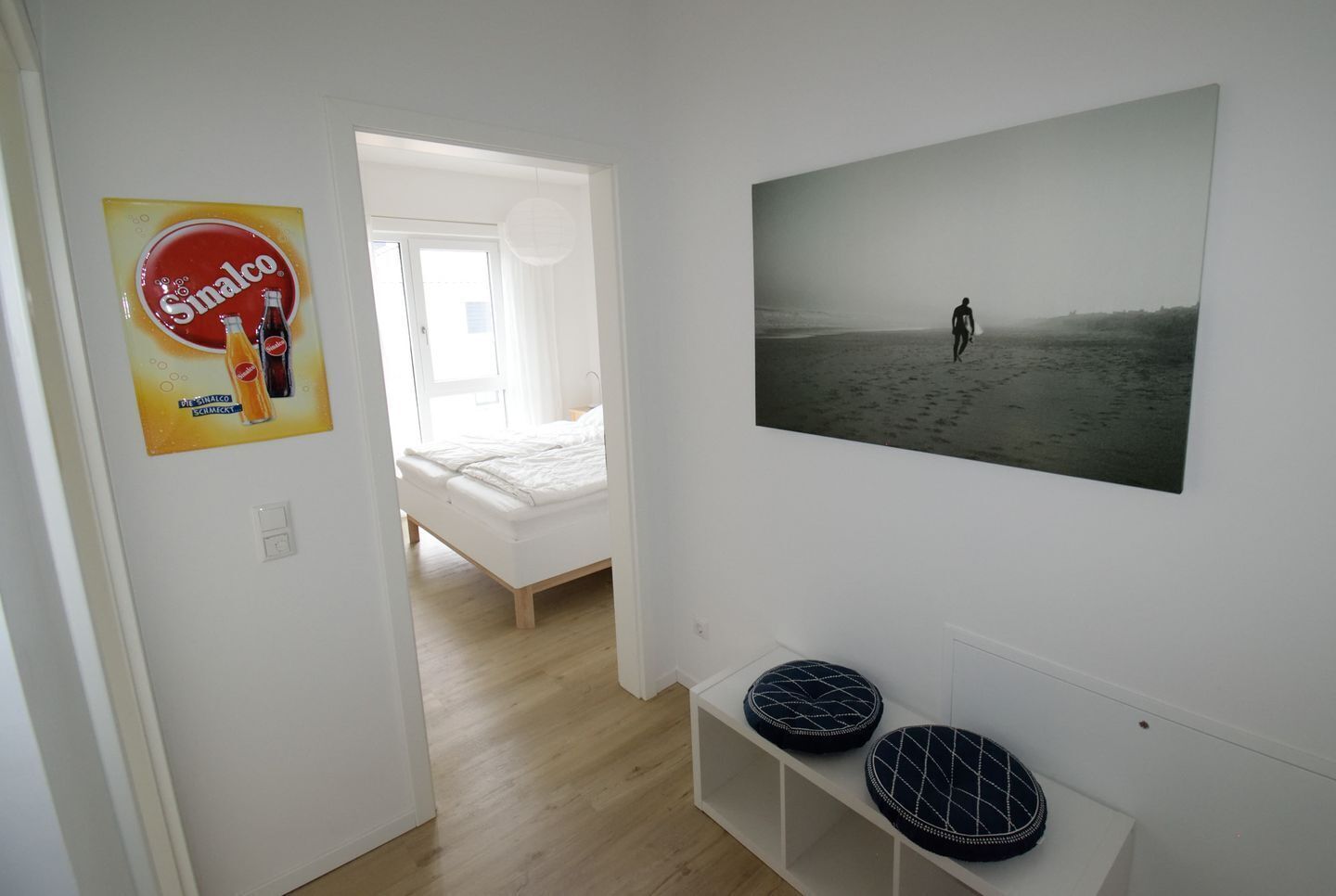 A bedroom with a bed, a poster of a beach scene, and a shelf with two decorative items.
