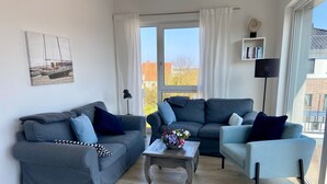 Un salon moderne avec deux canapés gris, une petite table sur laquelle est posé un vase de fleurs et une bibliothèque remplie de livres.