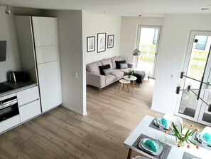 Une cuisine moderne avec des meubles blancs, un coin repas avec une table dressée pour deux personnes, et un salon avec un canapé et une table basse.