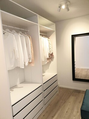Un dressing avec espace pour suspendre les vêtements et des tiroirs, un miroir et un plancher en bois.