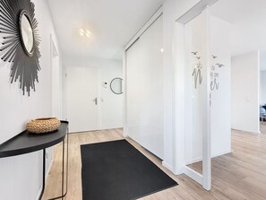 A modern interior with a black rug, a woven basket, a wall-mounted mirror, and a door with a circular mirror.