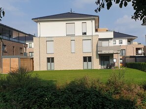 Een modern woongebouw met twee verdiepingen, een plat dak, grote ramen en een zichtbaar balkon.
