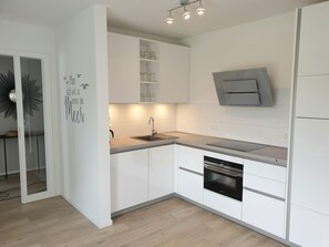 Une cuisine moderne avec des meubles blancs, un four encastré et un micro-ondes fixé au mur.