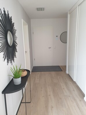 A hallway with a white door, a black wall-mounted mirror, a potted plant, and a black console table.