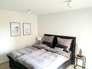 Een bed met een donker hoofdbord, een nachtkastje met een lamp, en twee ingekaderde foto's aan de muur.