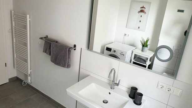 Un bagno moderno con lavabo bianco, specchio, porta asciugamani e lavatrice a incasso.