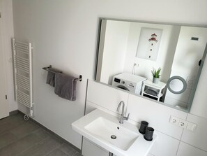 Un baño moderno con lavamanos blanco, espejo, toallero y lavadora integrada.
