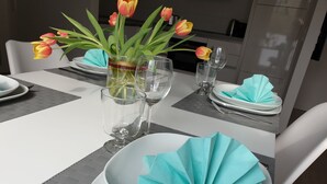 Une table à manger dressée avec de l’argenterie blanche, de la verrerie transparente et un vase rempli de tulipes.