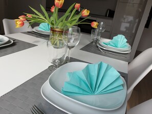 Een eettafel gedekt met witte borden, glazen en een vaas met tulpen.