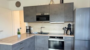 Una cocina moderna con armarios grises, un refrigerador de acero inoxidable, horno empotrado y cafetera.